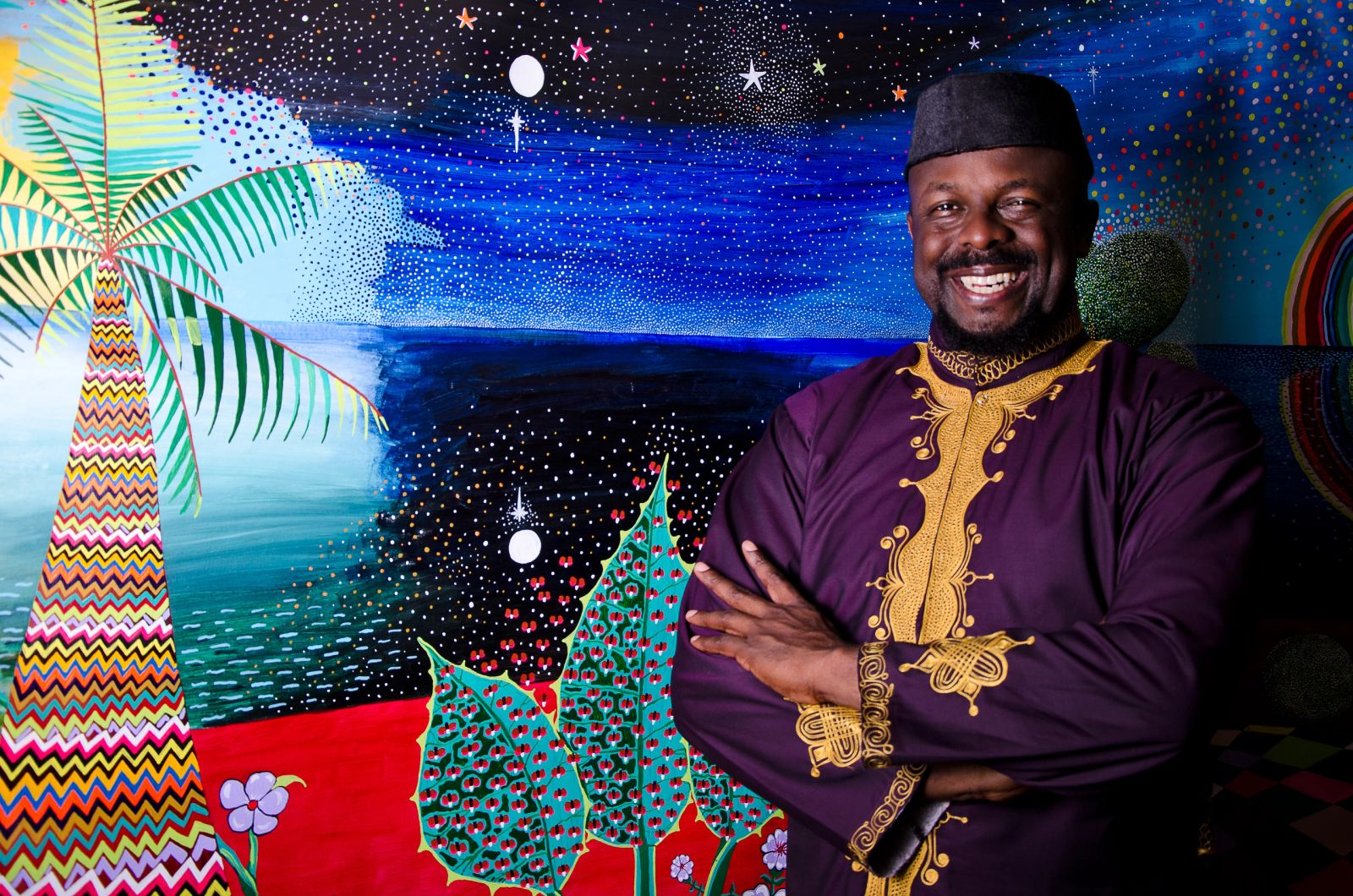Ibiyinka Alao seated with bright paintings in the background.
